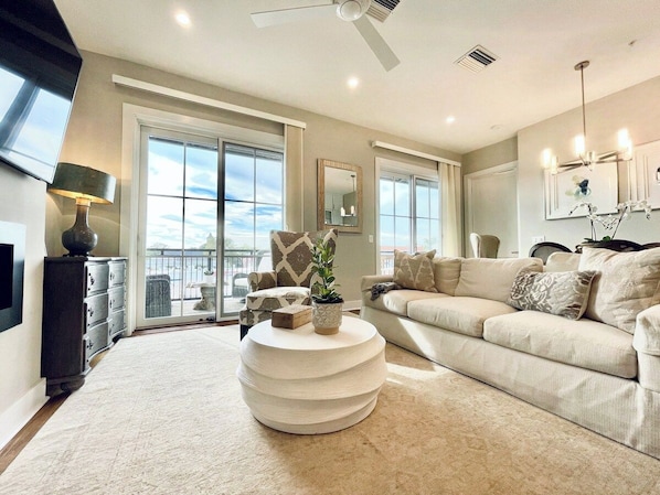 A spacious living room with a large window, a round coffee table, a sofa, and a TV.