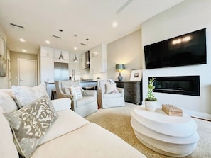 A modern living room with a sofa, armchairs, a coffee table, and a flat-screen TV mounted on the wall.