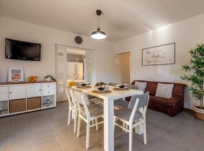 Ein moderner Essbereich mit einem weißen Tisch und Stühlen, einem flachbildfernseher an der Wand und einer Wanduhr.