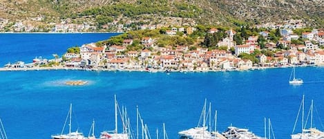 A coastal town with a marina filled with boats, surrounded by hills and clear blue waters.