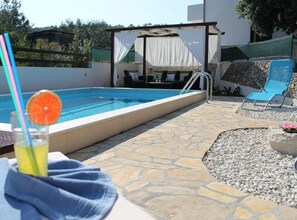 Ein Pool mit einer Steinterrasse, einer Liege und einem Tisch mit einem Getränk.