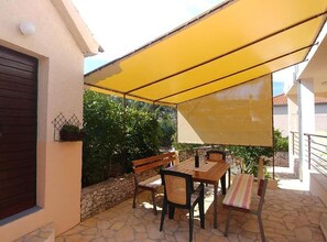 Eine Terrasse im Freien mit Tisch und Stühlen, einem gelben Sonnensegel und einer Steinmauer.