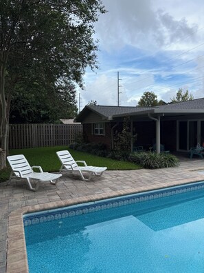A backyard with a swimming pool, two lounge chairs, a wooden fence, and a small brick building. - Home in the heart of Fort Walton Beach with private pool, minutes fromthe beach (Fort Walton Beach)