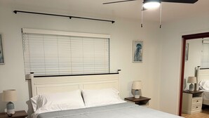 A bedroom with a bed, bedside tables, a ceiling fan, a window with blinds, and a mirror. - Home in the heart of Fort Walton Beach with private pool, minutes fromthe beach (Fort Walton Beach)