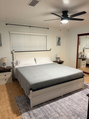 A bedroom with a bed, bedside tables, a ceiling fan, a window with blinds, and a mirror. - Home in the heart of Fort Walton Beach with private pool, minutes fromthe beach (Fort Walton Beach)