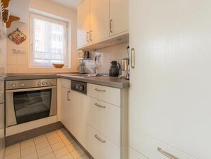 A kitchen with white cabinets, a built-in oven, a dishwasher, and a window with curtains. - 3 in the House at Blanker-hans-weg 5 (St. Peter-Ording)