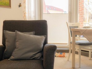 A room with a grey armchair, a white table with a plate and glass, and a window with blinds. - 3 in the House at Blanker-hans-weg 5 (St. Peter-Ording)