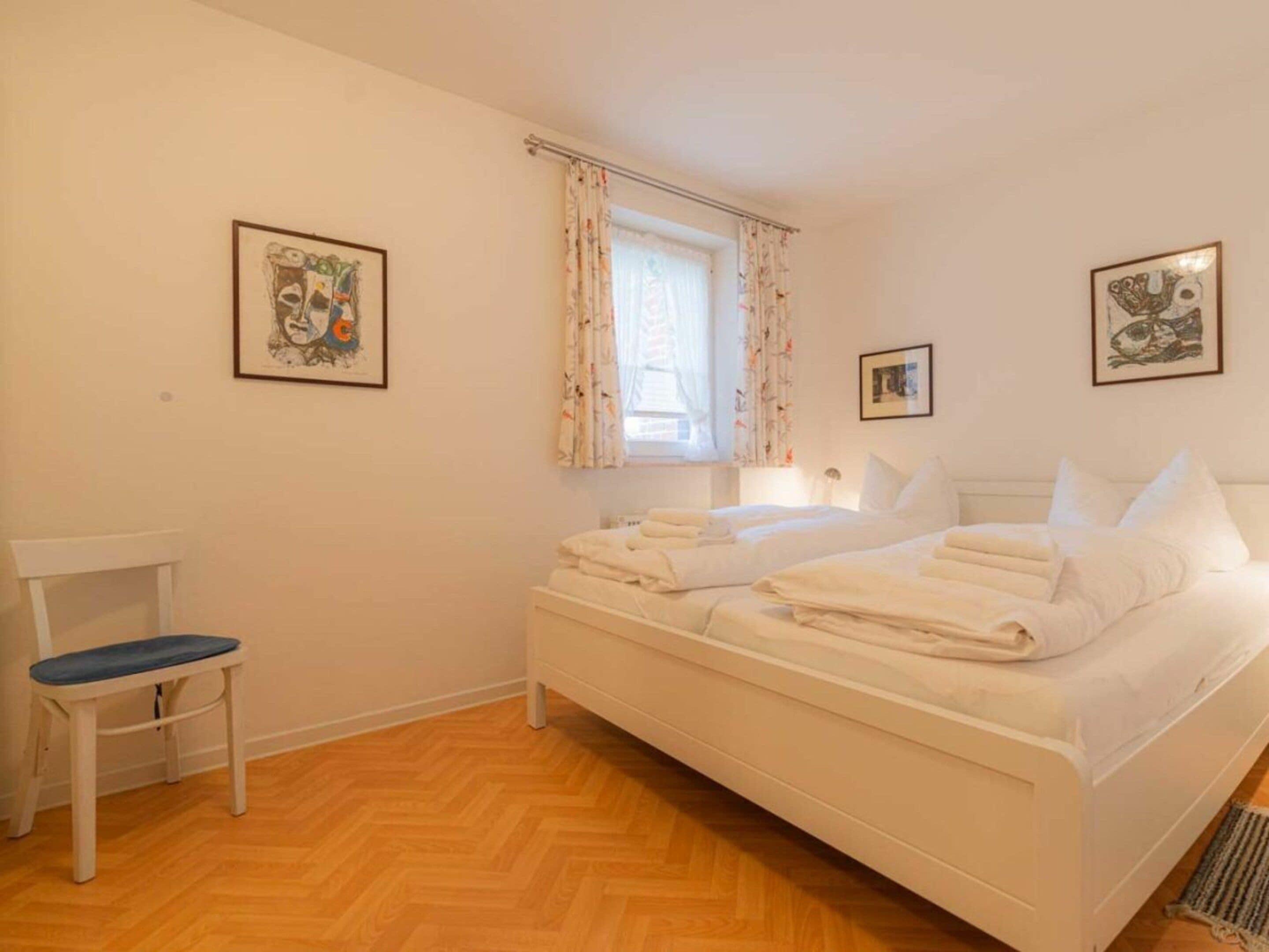 Een slaapkamer met een bed, een stoel en twee afbeeldingen in lijsten aan de muur.