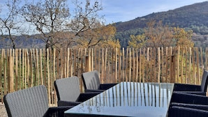 Un área de estar al aire libre con una mesa y sillas, rodeada por una cerca de madera y vistas a un paisaje montañoso.