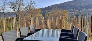 An outdoor seating area with a table and chairs, surrounded by a wooden fence, overlooking a hilly landscape. - Riviera Countryside Family Villa (Le Bar-sur-Loup)