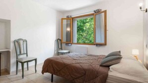 Un dormitorio con cama, una silla, un escritorio y una ventana con vistas a zonas verdes.