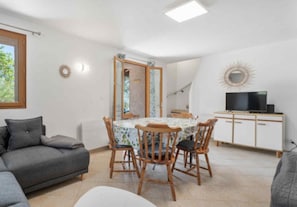A living room with a grey sofa, a dining table with chairs, a TV on a cabinet, and a mirror on the wall. - Riviera Countryside Family Villa (Le Bar-sur-Loup)