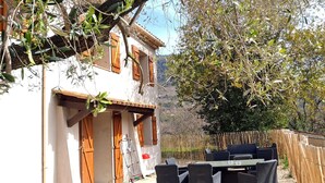Un edificio blanco con persianas de madera, un patio con mobiliario de mimbre y una valla de bambú.