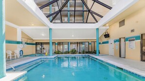 En indendørs swimmingpool med krystalklart blåt vand, et loft med geometrisk design og udsigt over bygningens indre.