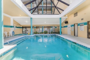 Una piscina interna con acqua cristallina, un soffitto con motivo geometrico e vista sull'interno dell'edificio.