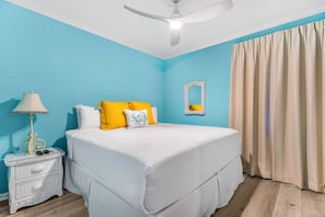 Una camera da letto con un letto, un comodino, una lampada, una ventola a soffitto e una finestra con tende.