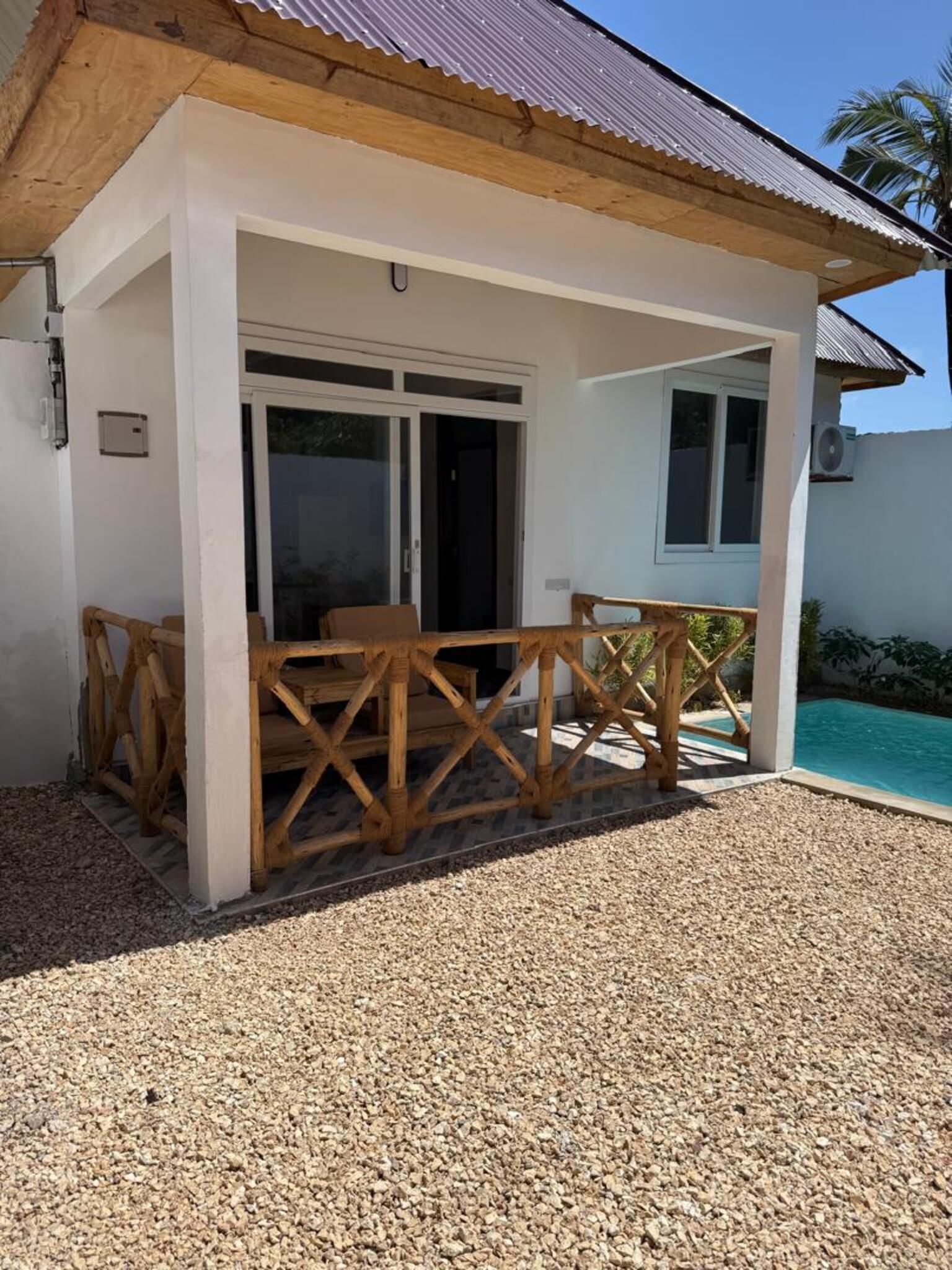 Uma área de estar coberta ao ar livre, com uma piscina ao fundo.