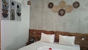 Habitación de hotel con una cama, un ventilador de techo, una pared con adornos y una mesita de noche con un teléfono.