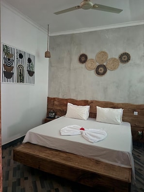 Quarto de hotel com cama, ventilador de teto, parede decorada e mesa de cabeceira com telefone.