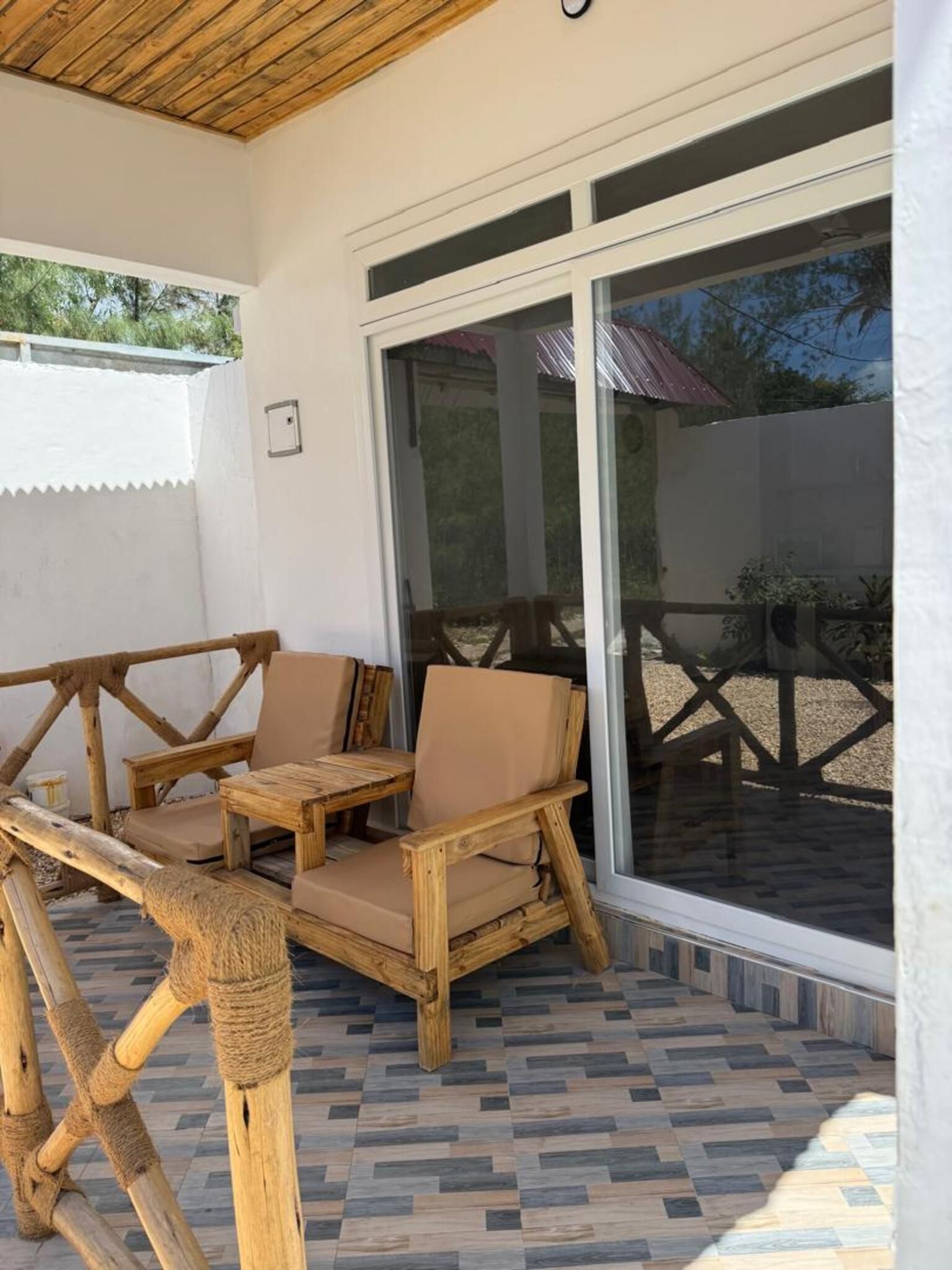 A covered patio area with a wooden table and chairs, a glass door leading outside, and a patterned floor.