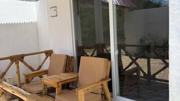 A covered patio area with a wooden table and chairs, a glass door leading outside, and a patterned floor.