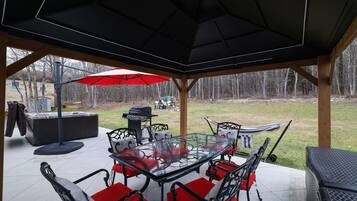 Un patio exterior con una mesa de vidrio, sillas rojas acolchadas, una parrilla y un paraguas rojo.