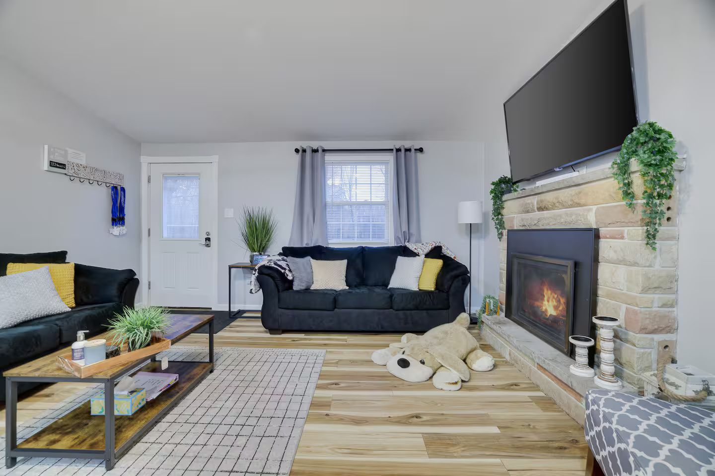 A living room with a black sofa, a coffee table, a fireplace, and a large TV.