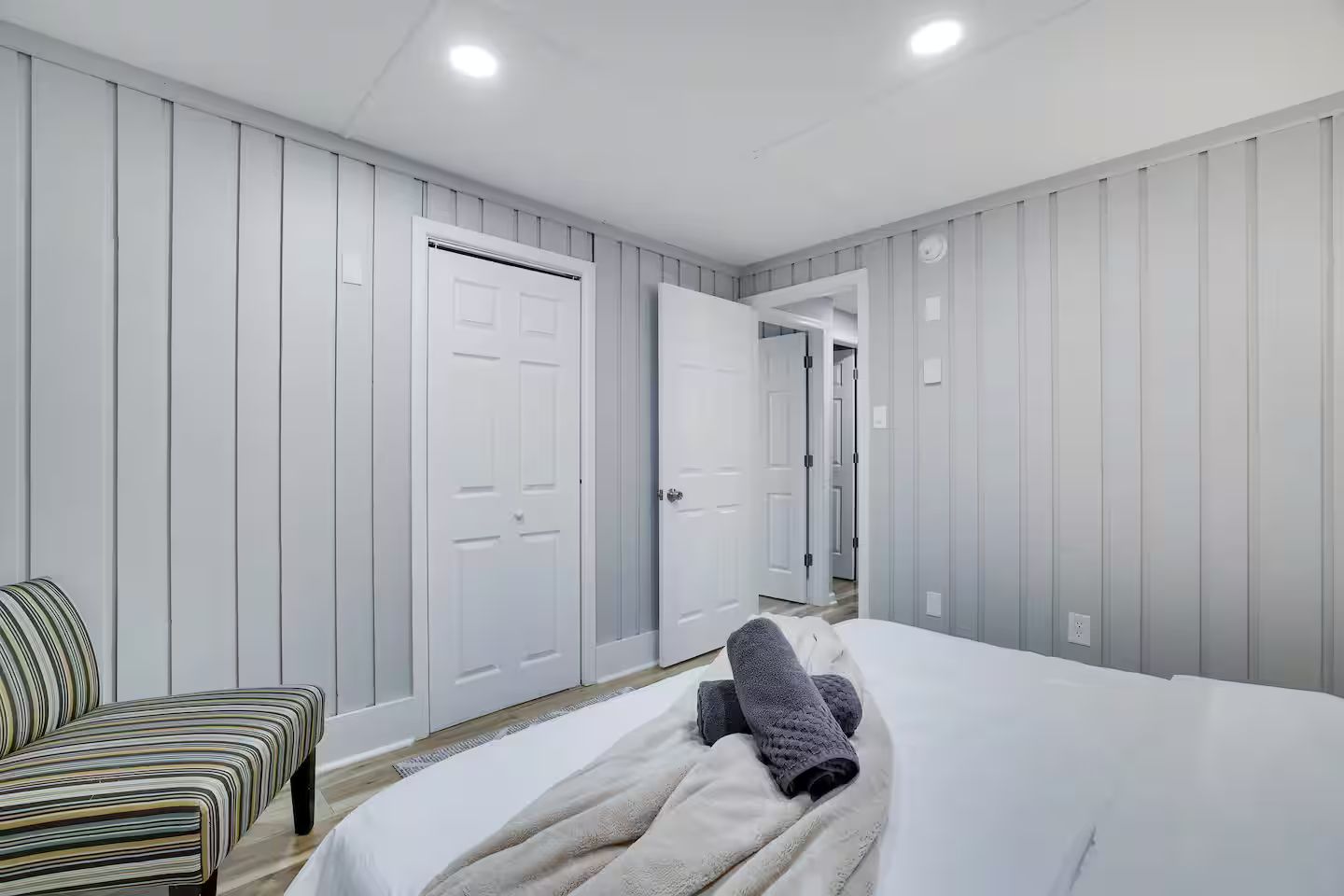 A hotel room with a bed, a chair, and two doors leading to other rooms.