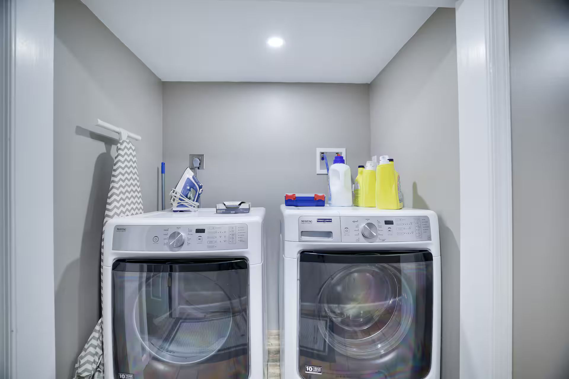 A laundry room with two front-loading washing machines, a towel rack, and cleaning supplies.