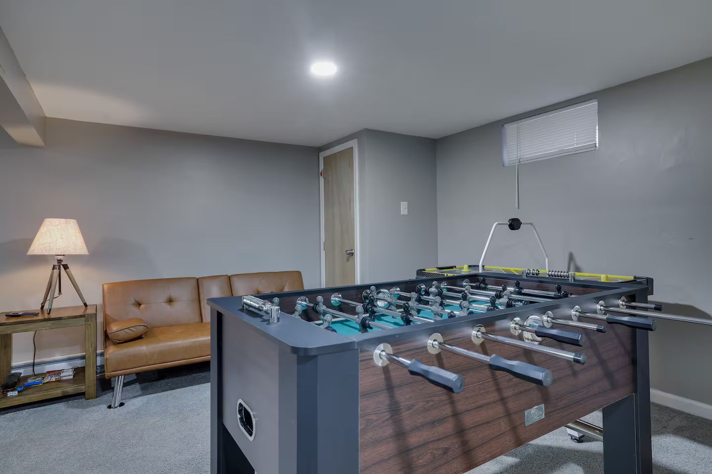 A room with a foosball table, a sofa, a lamp, and a door.