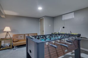 Ein Zimmer mit einem Fußballtisch, einer Couch, einer Lampe und einer Tür.