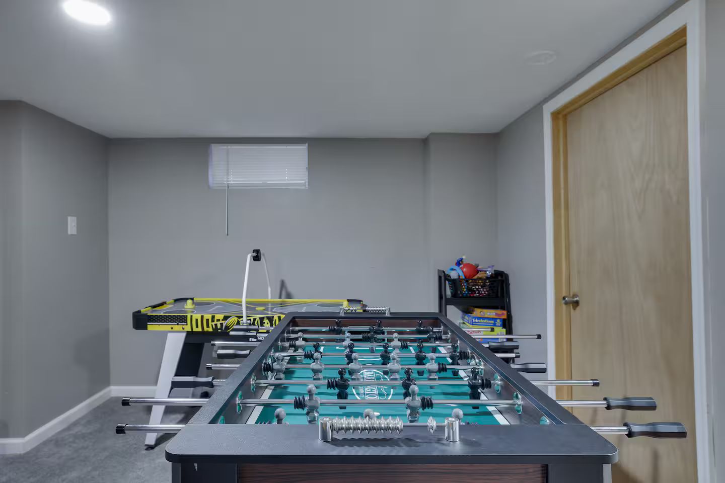 A room with a foosball table, a window, and a door.