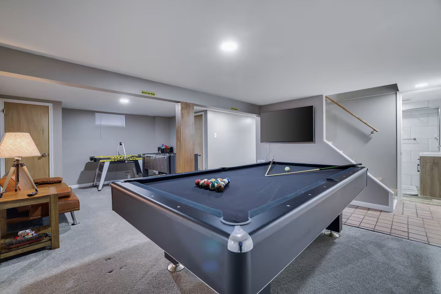 A pool table in a room with a sofa, a lamp, and a television mounted on the wall.