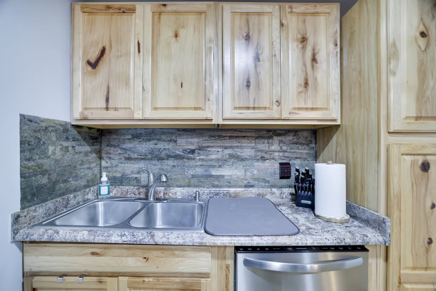 Una cocina con armarios de madera, encimera de granito, pileta doble y lavavajillas.
