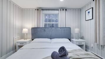 Une chambre d’hôtel avec un lit, deux tables de chevet, une fenêtre avec des stores et un tableau encadré au mur.