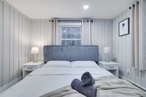 Una habitación de hotel con una cama, dos mesitas de noche, una ventana con persianas y un cuadro en la pared.