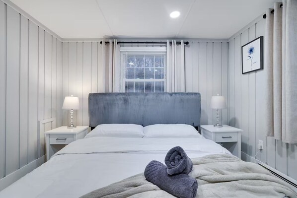 A hotel room with a bed, two bedside tables, a window with blinds, and a framed picture on the wall.