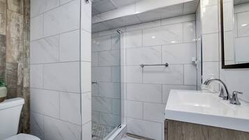 A modern bathroom with a glass-enclosed shower, a white sink, and a wooden accent wall.