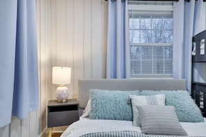 Ein Schlafzimmer mit einem Bett, einem Nachttisch mit Lampe und einem Fenster mit Jalousien.