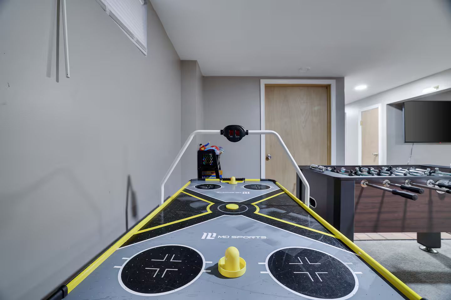 Una mesa de futbolín en una habitación con una puerta y un televisor montado en la pared.