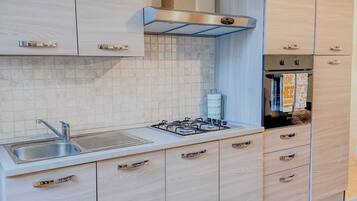 A modern kitchen with light wood cabinetry, a stainless steel range hood, a gas stove, and a built-in oven.