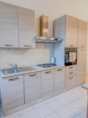Een moderne keuken met lichte houten kastjes, een roestvrijstalen afzuigkap, een gasfornuis en een inbouwoven.