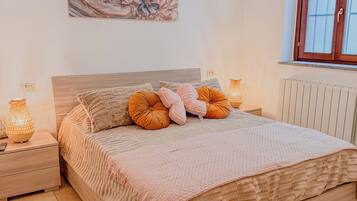 A bedroom with a wooden bed, a nightstand with a lamp, a wall-mounted air conditioner, and a window with a wooden frame.