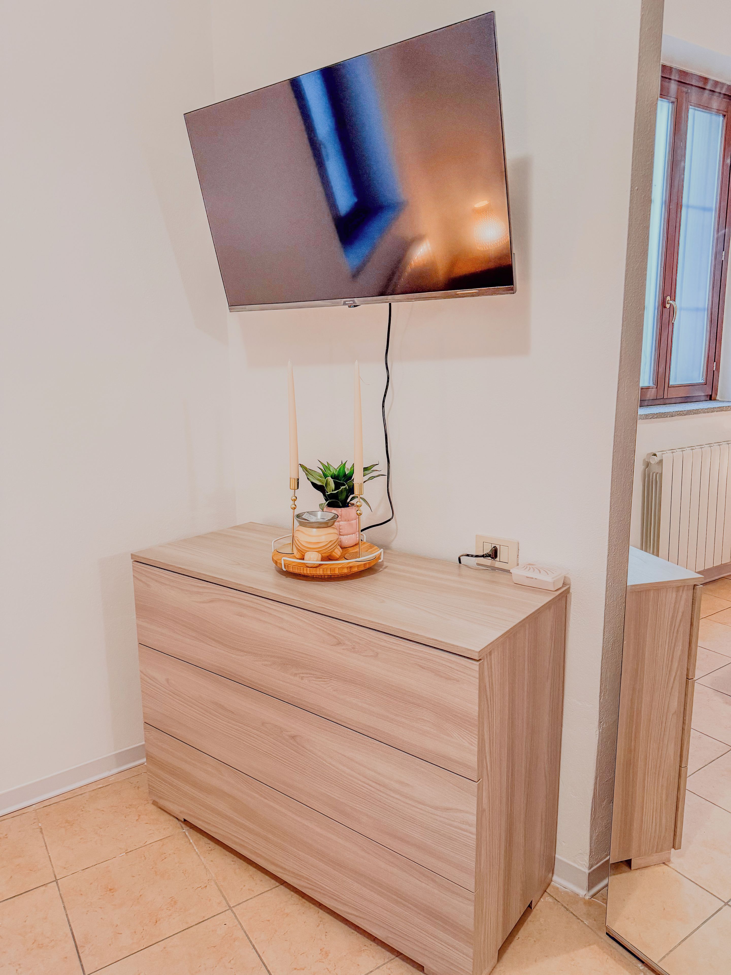 A modern room with a flat-screen TV mounted on the wall, a wooden cabinet with drawers, and a small potted plant on top.