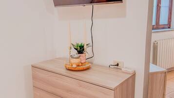 A modern room with a flat-screen TV mounted on the wall, a wooden cabinet with drawers, and a small potted plant on top.