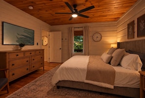 A bedroom with a bed, a dresser, a ceiling fan, a clock, and a window with curtains. - Luxe Cozy Creekfront Cottage | Bailey Creek Cabin (Marietta)