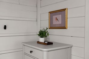 A white dresser with a drawer, a potted plant, and a framed picture on the wall. - Luxe Cozy Creekfront Cottage | Bailey Creek Cabin (Marietta)