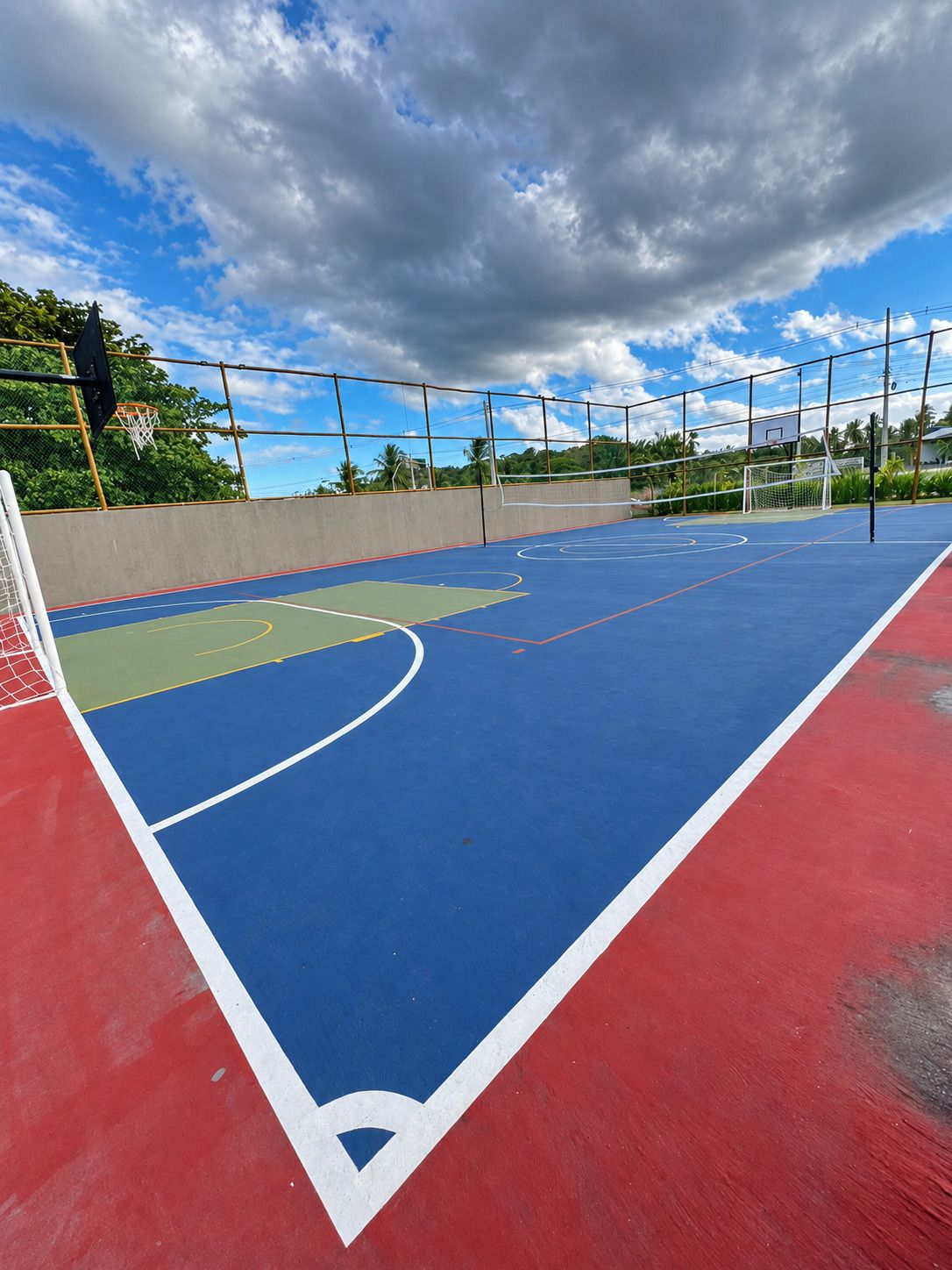 Una cancha de baloncesto al aire libre con superficie azul, borde rojo y línea blanca que delimita el área de la llave.