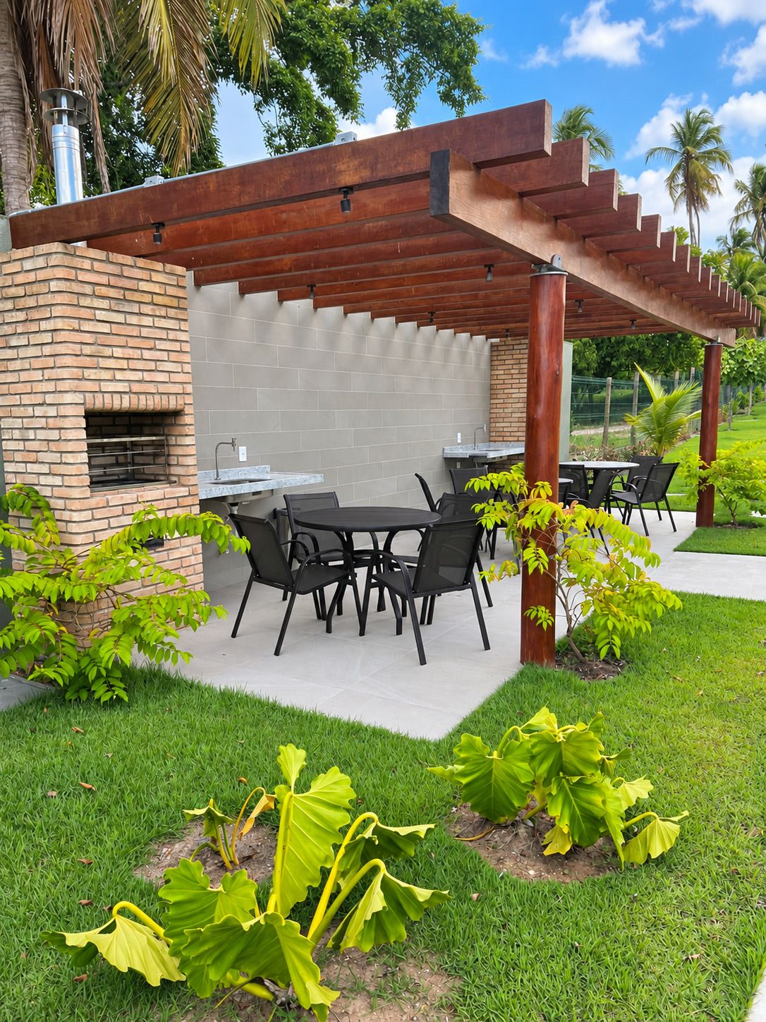 Un patio exterior con pared de ladrillo, una pérgola y un área de estar con mesas y sillas.