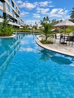 Una piscina con suelo de baldosas, rodeada de palmeras y un edificio de varios pisos.